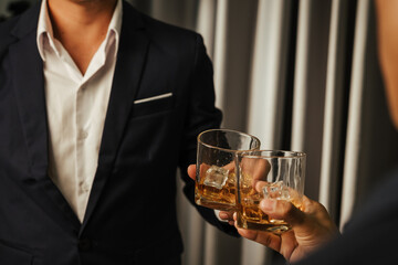 A stylish man holds a glass of whiskey at an upscale bar, enjoying a luxurious indoor celebration with friends and fine alcohol.