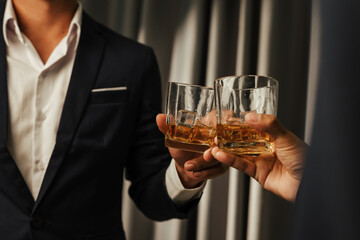 A stylish man holds a glass of whiskey at an upscale bar, enjoying a luxurious indoor celebration with friends and fine alcohol.