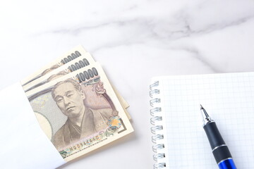 福沢諭吉の肖像の一万円紙幣とメモ帳、ペン
