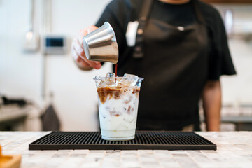 Barista pours espresso into iced milk for a refreshing latte in a modern café. Close-up shows swirling coffee layers and craft beverage preparation, ideal for food, drink, and small business themes.