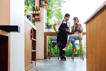 Cafe owner consults with financial advisor using smartphone, seated in modern coffee shop. Scene...