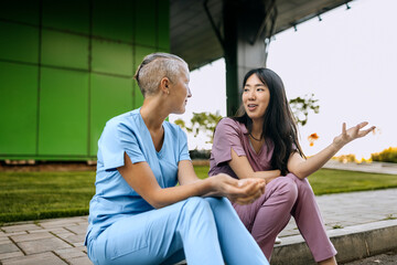 Nurses engaged in friendly conversation during break in outdoor setting at healthcare facility