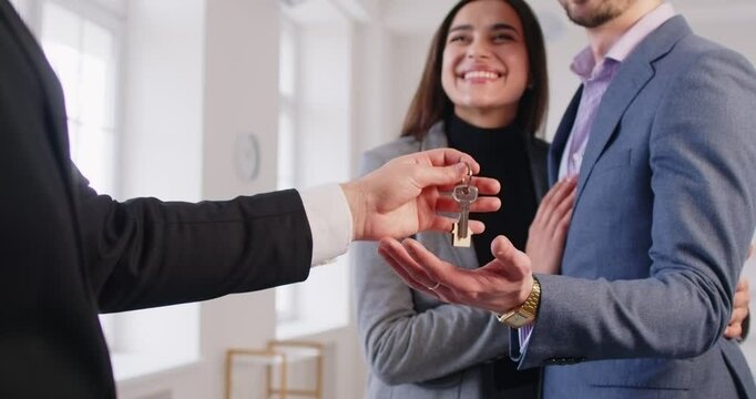 Happy young couple owners receiving keys from new own property flat, finish meeting in real estate agency realtor, bank mortgage for family, selling, renting, celebrating enjoyable contract 