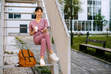 Nurse enjoying a break outside while checking her phone and sipping a drink on a sunny day