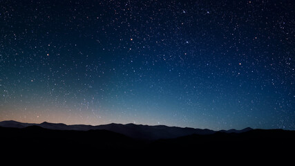 a a movement of stars in the night sky with the view of mountains.