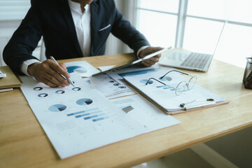 A businesswoman sits at a desk in a corporate office, analyzing financial documents, charts, and...