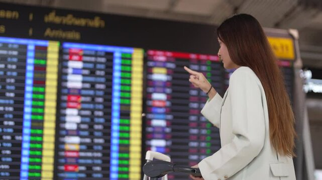 Confident businesswoman at airport terminal with suitcase checking departure board ready for first class travel, professional look waiting flight in luxury business trip, premium international travel