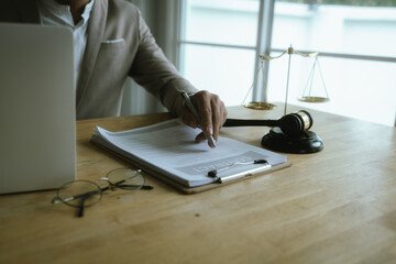A professional woman lawyer sits at her desk in an office, reviewing legal documents with a gavel and law books nearby.