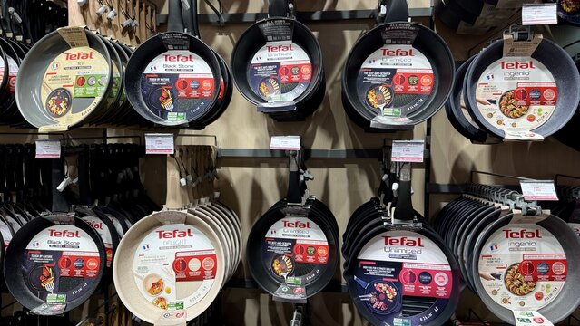 Tefal cookware and appliances store display featuring numerous non-stick frying pans arranged neatly on well-lit retail shelves..