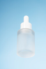 White unbranded dropper bottle on glass against blue background. Skin care product presentation. Trendy showcase . bottom view