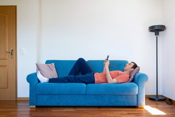 Caucasian male lying down on a sofa or couch, holding and looking at his smart phone