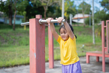 Obraz premium Asian Young Girl Engaging in Outdoor Physical Activity at Playground, Focused on Strength Training and Fitness, Promoting Healthy Active Lifestyle for Children