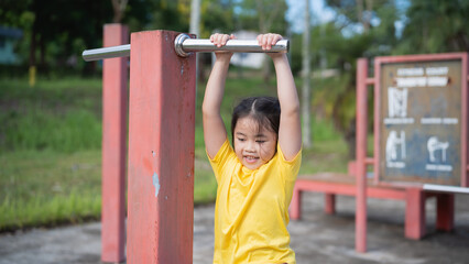 Fototapeta premium Asian Young child practicing grab pull-up on playground bars in vibrant yellow shirt, showcasing strength and determination in outdoor fitness area