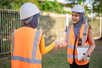 Muslim women engineers checking hands construction together. Both wear protective vests and...