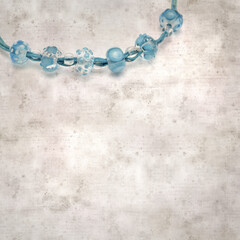 textured stylish old paper background, square, with a simple necklace of blue and transparent glass...