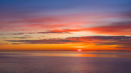 Obraz premium Vibrant Sunset over Calm Ocean Water with Dramatic Sky