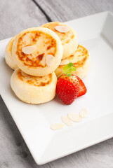 Delicious sweet cottage cheese pancakes served with fresh strawberries and cream on a white plate for breakfast