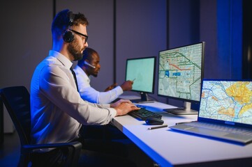 Male Data Scientist Works on Personal Computer Wearing a Headset in Big Infrastructure Control and...