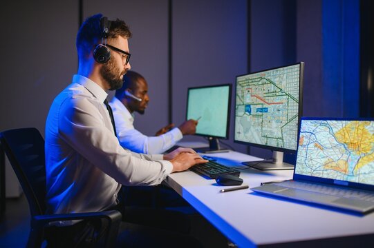 Male Data Scientist Works on Personal Computer Wearing a Headset in Big Infrastructure Control and Monitoring Room