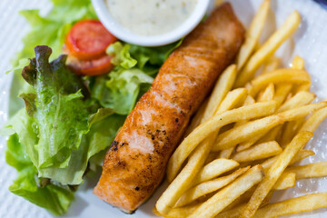 Plate of grilled salmon steak served with vegetables and french fries. Overhead view