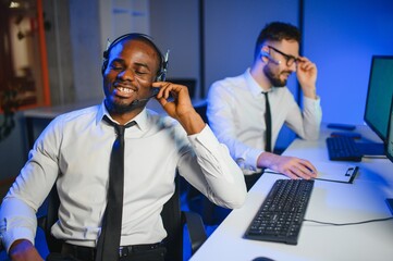 Male Data Scientist Works on Personal Computer Wearing a Headset in Big Infrastructure Control and...