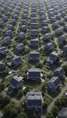 Aerial view of suburban neighborhood with rows of houses featuring solar panels on their roofs, surrounded by green lawns and trees, showcasing sustainable living