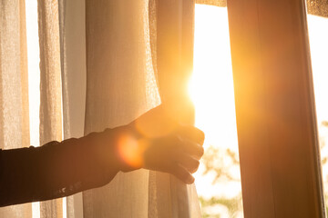 woman's hand She opened the curtains on the window. There was morning light through the window in her room, looking at the view of the mountains and trees as the sun rose	