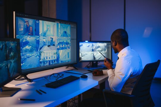 African American security officer or dispatch uses computer and walkie talkie, looks at screens