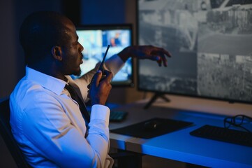 Back view of African American security operator use computer with screens showing surveillance...