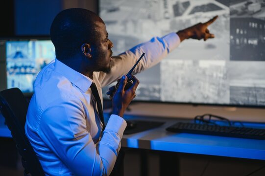 African-American security officer watching the screens talking on radio in control room