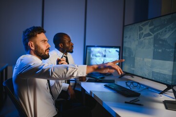 Two male security guards looking at computer screen while one of them explaining detail of video