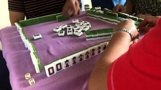 Family members are spending time playing the game of mahjong together at the table
