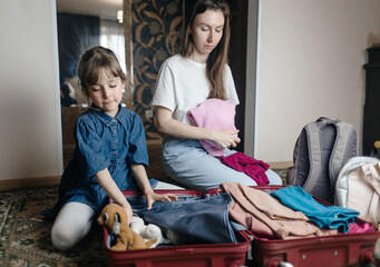 Tired mother with 6 year old daughter packing travel suitcase. Travel concept. Close-up of travel bag and tired faces of travelers.