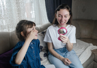 Daughter puts makeup on her mother face and plays around. Caring parent allows her child to paint her face. Happy childhood. Concept of loving family and fun. little girl doing her makeup