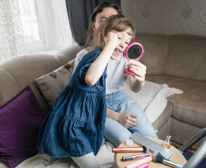 Daughter puts makeup on her mother face and plays around. Caring parent allows her child to paint her face. Happy childhood. Concept of loving family and fun. little girl doing her makeup