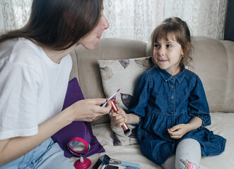 Mother putting makeup on her daughter face and they fool around together. Communication between women in the family. Fun time. Happy family concept. little girl doing her makeup