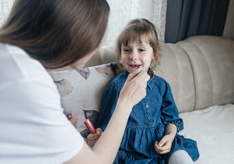 Mother putting makeup on her daughter face and they fool around together. Communication between women in the family. Fun time. Happy family concept. little girl doing her makeup