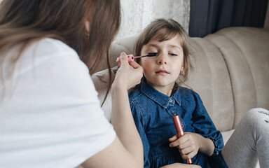 Mother putting makeup on her daughter face and they fool around together. Communication between women in the family. Fun time. Happy family concept. little girl doing her makeup
