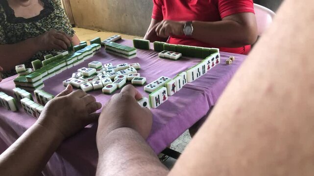 Family members are spending time playing the game of mahjong together at the table