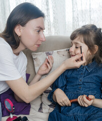Mother putting makeup on her daughter face and they fool around together. Communication between women in the family. Fun time. Happy family concept. little girl doing her makeup
