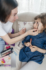 Mother putting makeup on her daughter face and they fool around together. Communication between women in the family. Fun time. Happy family concept. little girl doing her makeup