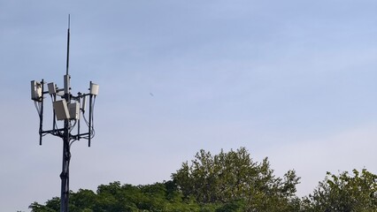 Tower with antennas for telecommunications against a clear blue sky and green foliage below