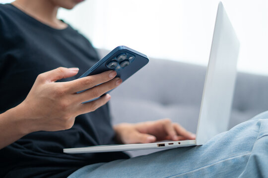 Close-up view of woman working from home using smartphone and laptop through internet communication network technology and e-commerce marketing.