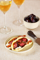 Fresh farm cheese roll with dates, freeze-dried strawberries and cream cheese in a plate with a glass of white non-alcoholic wine. Vertical orientation.