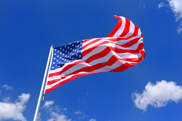 The flag of  United States flutters in the wind in a blue sky with white clouds