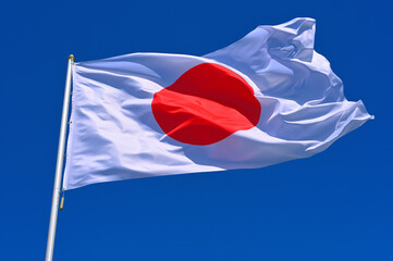 The flag of  Japan flutters in the wind in a blue sky with white clouds