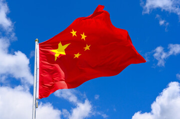 The flag of China  flutters in the wind in a blue sky with white clouds