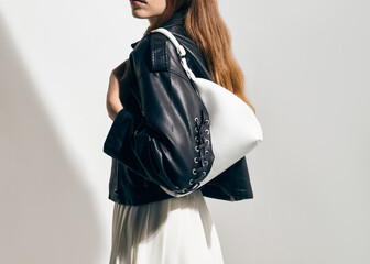 A stylish woman in a leather jacket with a bag in her hand poses against a light background