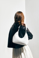 A stylish woman in a leather jacket with a bag in her hand poses against a light background