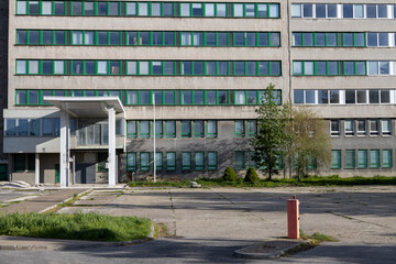 A wide view of an aging, utilitarian office or industrial building. The concrete facade appears worn and weathered. Urban decay, institutional design, and post-socialist cityscapes.